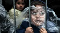 Seorang anak pengungsi tertutup jas hujan menunggu antrean mendapatkan kamp di Presevo, (7/10/2015). Foto ini pemenang '1st prize singles' World Press Photo Awards 2016 kategori People karya Matic Zorman berjudul 'Waiting to Register'. (Reuters via WPP)