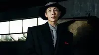 Lalu, Kim Namjoon atau RM mengenakan topi fedora dengan longcoat hitam detail kancing pesawat, kemeja bergaris dan dasi pun menjadi inner tampilannya. (Louis Vuitton)