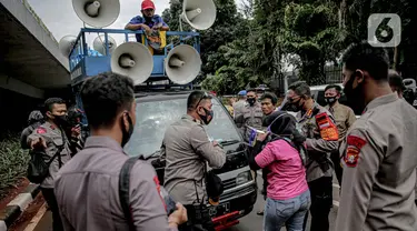 Petugas kepolisian beradu argumen saat memberhentikan mobil komando aksi di sekitar Gedung DPR, Jakarta, Jumat (14/8/2020). Polda Metro Jaya melarang adanya unjuk rasa di depan Gedung DPR/MPR yang bertepatan dengan sidang tahunan. (Liputan6.com/Faizal Fanani)
