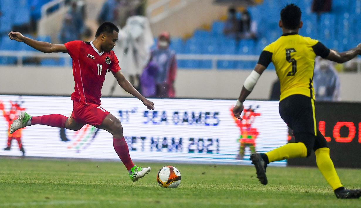 <p>Gelandang Timnas Indonesia U-23, Saddil Ramdani mencoba melepaskan tembakan dari kawalan bek Malaysia, Harith Haiqal bin Adam Afkar dalam pertandingan perebutan medali perunggu SEA Games 2021 di Stadion My Dinh, Minggu (22/5/2022). Indonesia ditahan imbang 1-1 dan menang 4-3 di adu penalti. (AFP/Ye Aung Thu)</p>