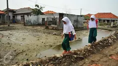 Dua orang siswi melewati pelataran bekas rumah yang terkena dampak abrasi di pantai Muara Gembong, Bekasi, Selasa, (26/7). Tingkat abrasi yang tinggi menyebabkan sejumlah rumah terkikis dan beberapa sekolah terendam air laut. (Liputan6.com/Gempur M Surya)