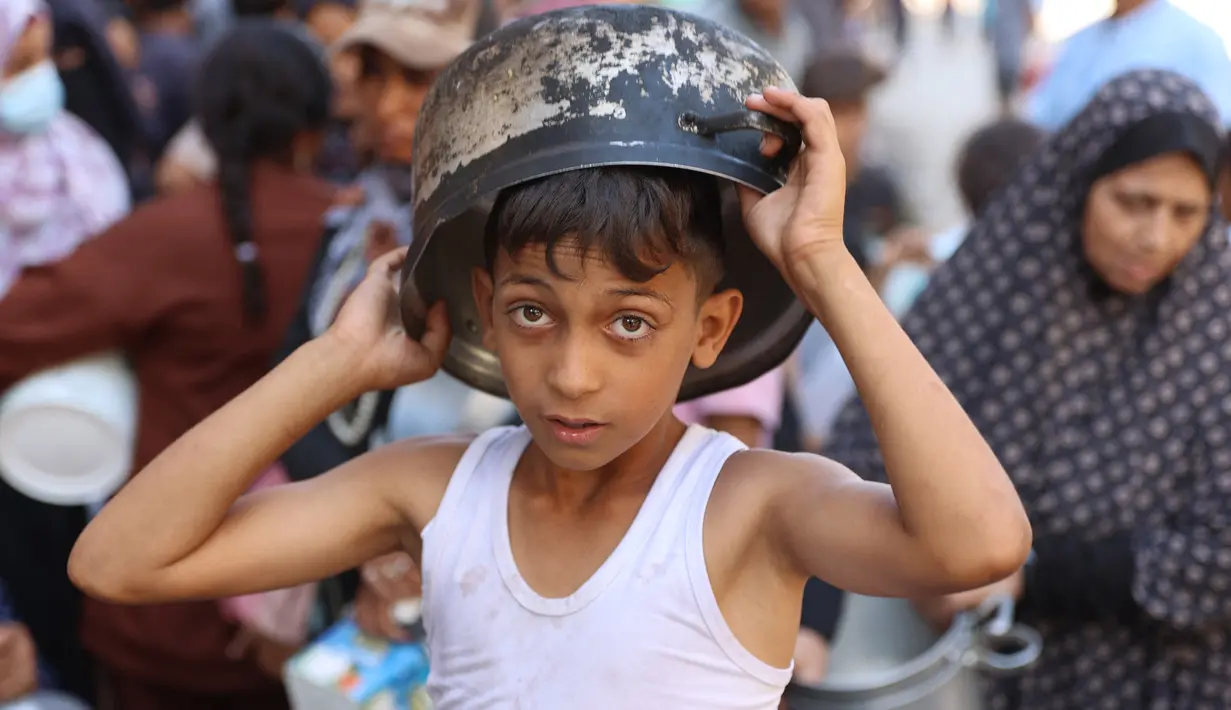 Seorang anak laki-laki Palestina mengantri untuk menerima jatah makanan, yang ditawarkan oleh sebuah badan amal, di kamp pengungsi Al-Shati di Gaza pada 17 Oktober 2024. (Omar AL-QATTAA/AFP)