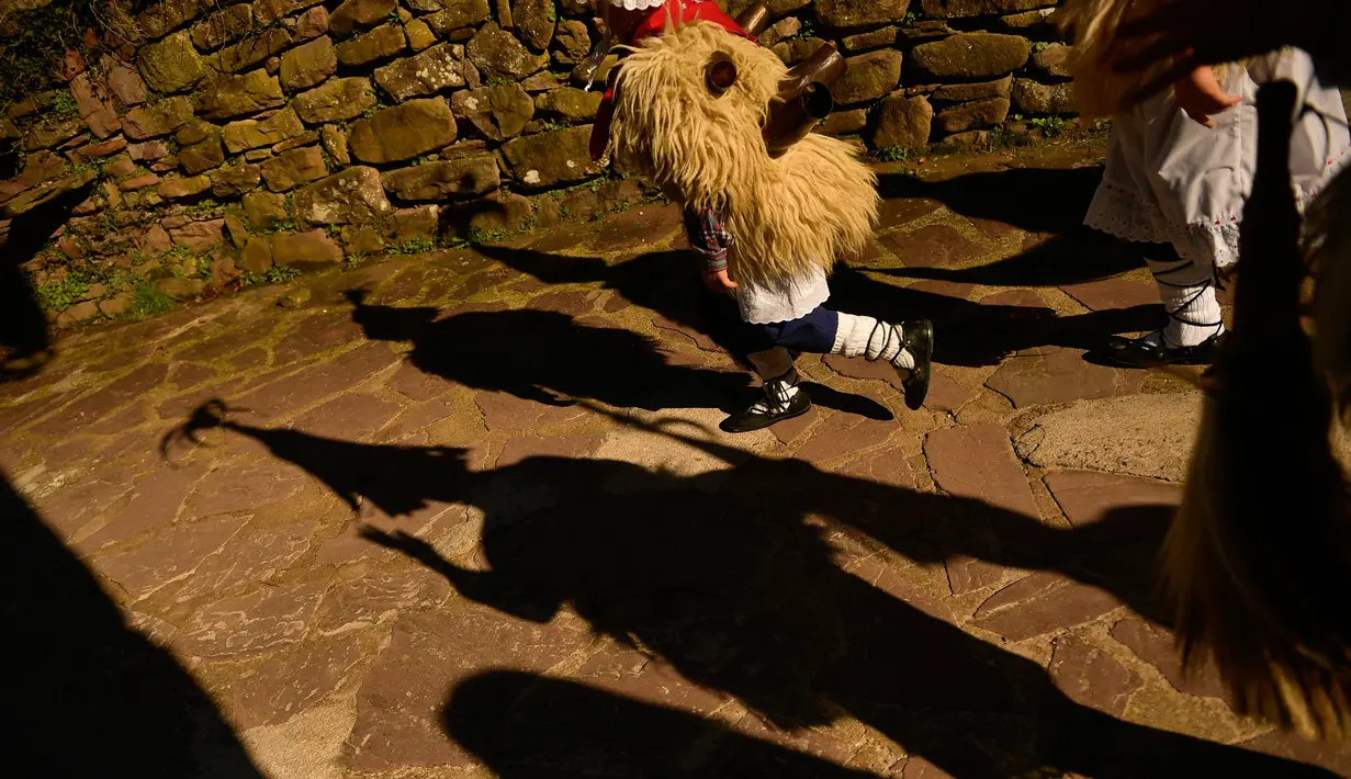 Seorang anak mengenakan kostum dengan latar belakang bayangan peserta karnaval di antara desa Pyrenees Ituren dan Zubieta, Spanyol (29/1). Acara ini merupakan salah satu karnaval paling kuno di Eropa. (AP Photo / Alvaro Barrientos)