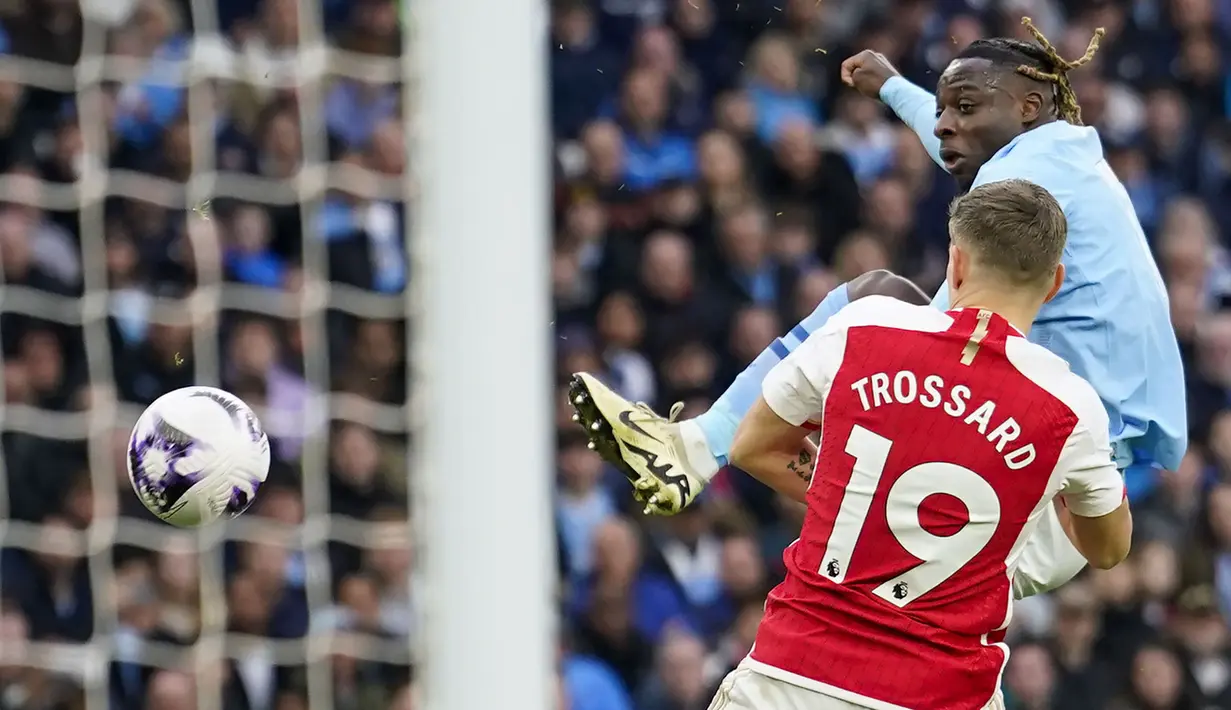 Gelandang Manchester City, Jeremy Doku (belakang) melepaskan tendangan di bawah tekanan gelandang Arsenal, Leandro Trossard pada laga pekan ke-30 Premier League 2023/2024 di Etihad Stadium, Manchester, Minggu (31/3/2024). (AP Photo/Dave Thompson)