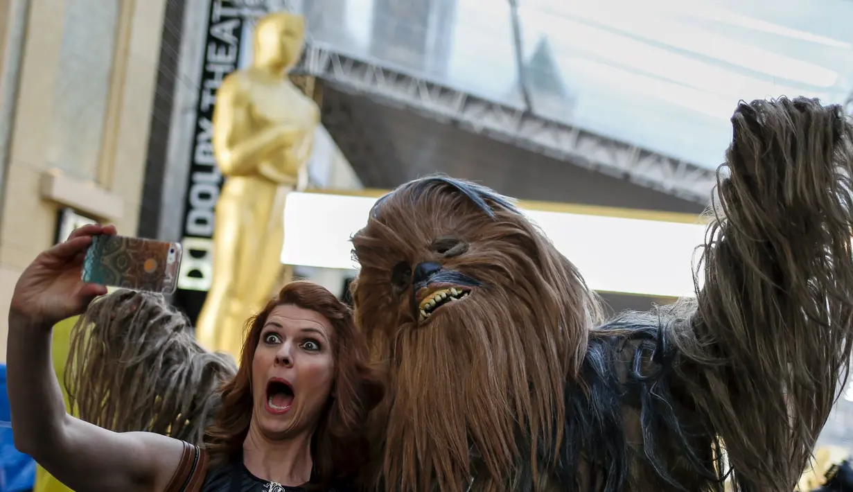 Seorang wanita berselfie bersama karakter Star Wars dengan latar belakang patung Oscar 2016 di luar Teater Dolby, Hollywood, California, Sabtu (27/2). Acara penghargaan Academy Awards ke-88 ini akan berlangsung pada Minggu (28/2). (REUTERS/Adrees Latif)