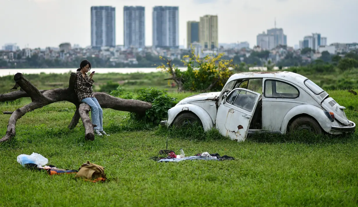 Seorang gadis memeriksa ponselnya sambil duduk di lapangan terbuka di sepanjang tepi sungai Merah di Hanoi (13/0/2020). (AFP/Manan Vatsyayana)