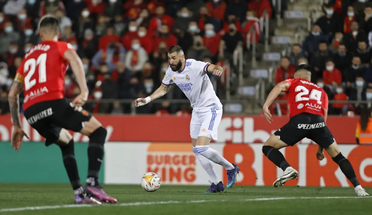 Penyerang Real Madrid, Karim Benzema membawa bola dari kawalan dua pemain Mallorca pada pertandingan lanjutan La Liga Spanyol di Palma de Mallorca, Spanyol, Selasa (15/3/2022). Madrid menang telak atas Mallorca 3-0. (AP Photo/Francisco Ubilla)