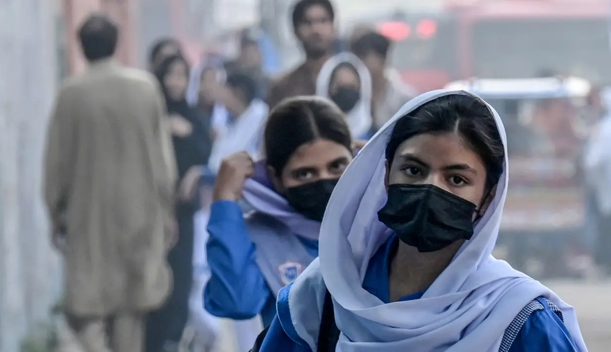 Para siswi sekolah yang mengenakan masker tiba di sebuah sekolah di tengah kondisi kabut asap di Lahore pada Senin 4 November 2024. (Arif ALI/AFP)