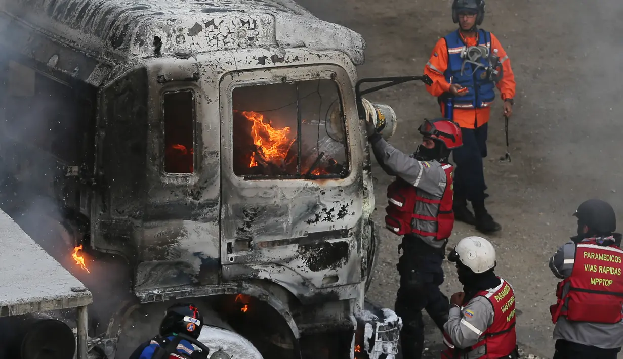 Petugas pemadam kebakaran berusaha memadamkan api dari truk yang dibakar para demonstran saat menggelar aksinya di Caracas, Venezuela (24/4). Dilaporkan kerusuhan berkepanjagan ini telah menewaskan sedikitnya 21 orang. (AP Photo/Fernando Llano)