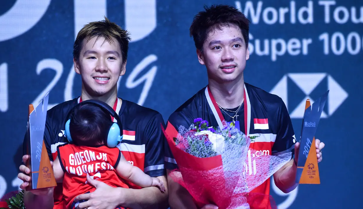Ganda putra Indonesia Marcus Fernaldi Gideon (kiri) mengendong putranya, Marcus Fernaldi Gideon Junior bersama Kevin Sanjaya Sukamuljo berpose usai pertandingan final ganda putra Indonesia Open 2019 melawan Mohammad Ahsan/Hendra Setiawan di Istora Senayan, Minggu (21/7/2019). (AFP Photo/Adek Berry)