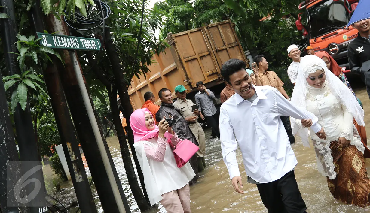 Pengantin Mansur dan Maya melintasi banjir usai melakukan akad nikah di KUA Mampang Prapatan, Jakarta, Selasa (21/2). Walaupun banjir sepasang pengantin ini tetap melakukan akad nikah. (Liputan6.com/Herman Zakharia)