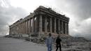 Pengunjung pertama yang mengenakan masker wberjalan di atas bukit Acropolis, dengan latar belakang kuil Parthenon di Athena, Senin (22/3/2021). Yunani membuka kembali Acropolis dan situs kuno lainnya secara nasional untuk memulai kembali musim pariwisata pada pertengahan Mei. (AP Photo/Th