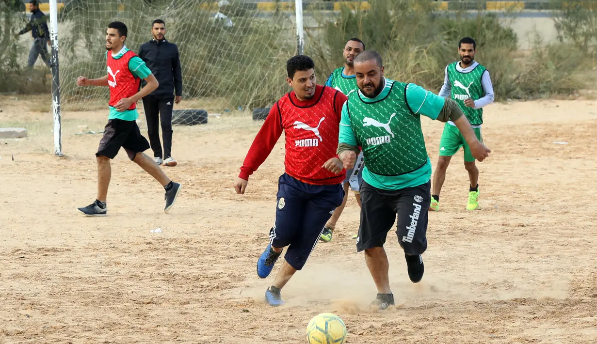 Dua pria berebut bola saat bermain di lapangan tanah sebelum buka puasa selama bulan Ramadhan, di ibu kota Libya, Tripoli (24/4/2021). (AFP/Mahmud Turkia)