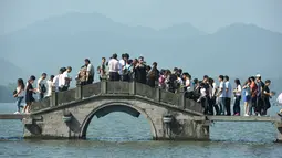 Pengunjung berjalan di sebuah jembatan di West Lake selama liburan di Hangzhou, Provinsi Zhejiang, Tiongkok, 2 Oktober 2016. Wisatawan menunggu datang gelombang besar yang akan menghantam pinggiran pantai. (REUTERS)