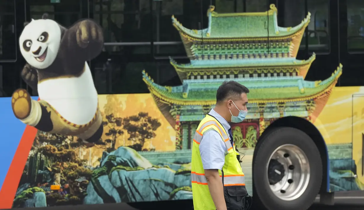 Petugas lalu lintas berdiri di dekat bus dengan iklan untuk taman hiburan Universal Studios selama uji coba di Beijing (31/8/2021). Perusahaan menetapkan tanggal pembukaan 20 September, menurut pernyataan dan video yang diposting di situs media sosial China WeChat. (AP Photo/Ng Han Guan)