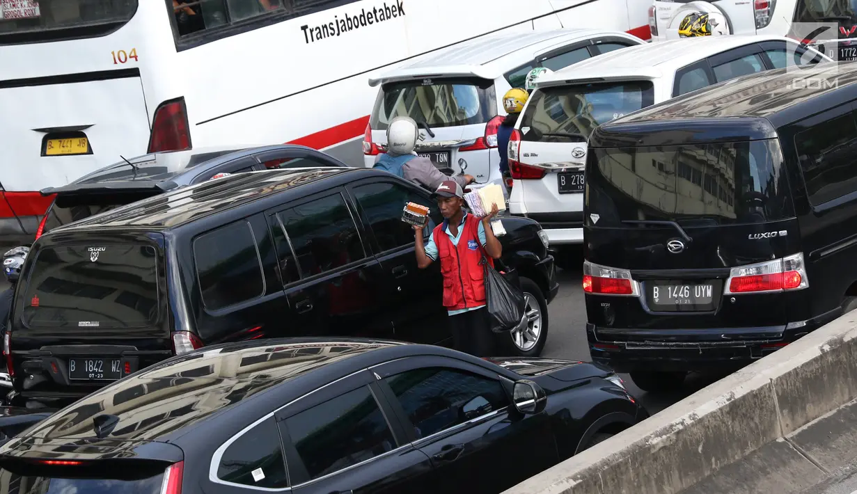 Pedagang asongan menjajakan barang dagangannya di persimpangan lampu merah di Jakarta, Jumat (22/2). Keahlian yang terbatas menyebabkan sebagian orang harus bekerja di tengah padatnya kendaraan Ibukota. (Liputan6.com/Immanuel Antonius)