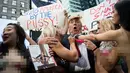 Seorang seninam berpenampilan seperti kandidat presiden AS dari Partai Republik Donald Trump melakukan aksi unjuk rasa dengan dikelilingi wanita-wanita seksi berbikini di depan Times Square, New York (25/10). (AFP Photo/Drew Angerer/Getty Images)