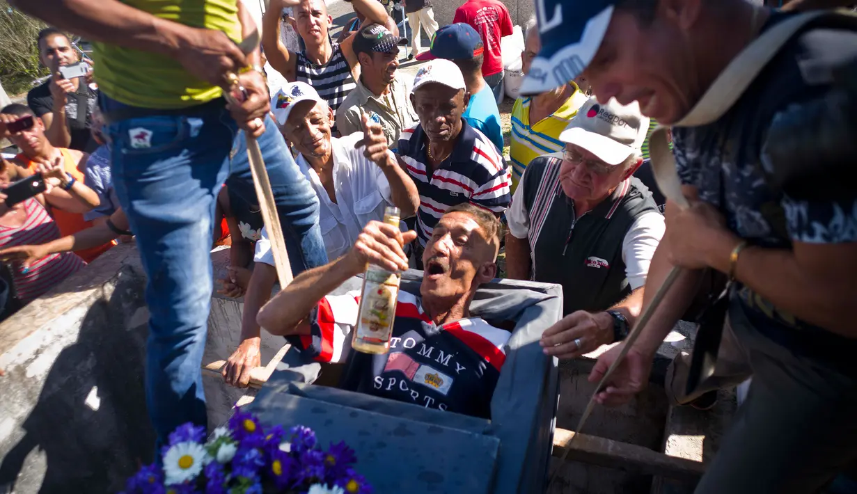 Divaldo Aguiar berbaring di dalam peti sambil meminum sebotol rum saat festival Burial of Pachencho di Santiago de Las Vegas, Kuba (5/2). Perayaan ini merupakan tardisi masyarakat setempat yang digelar setiap tangggal 5 Februari. (AP Photo/Ramon Espinosa)