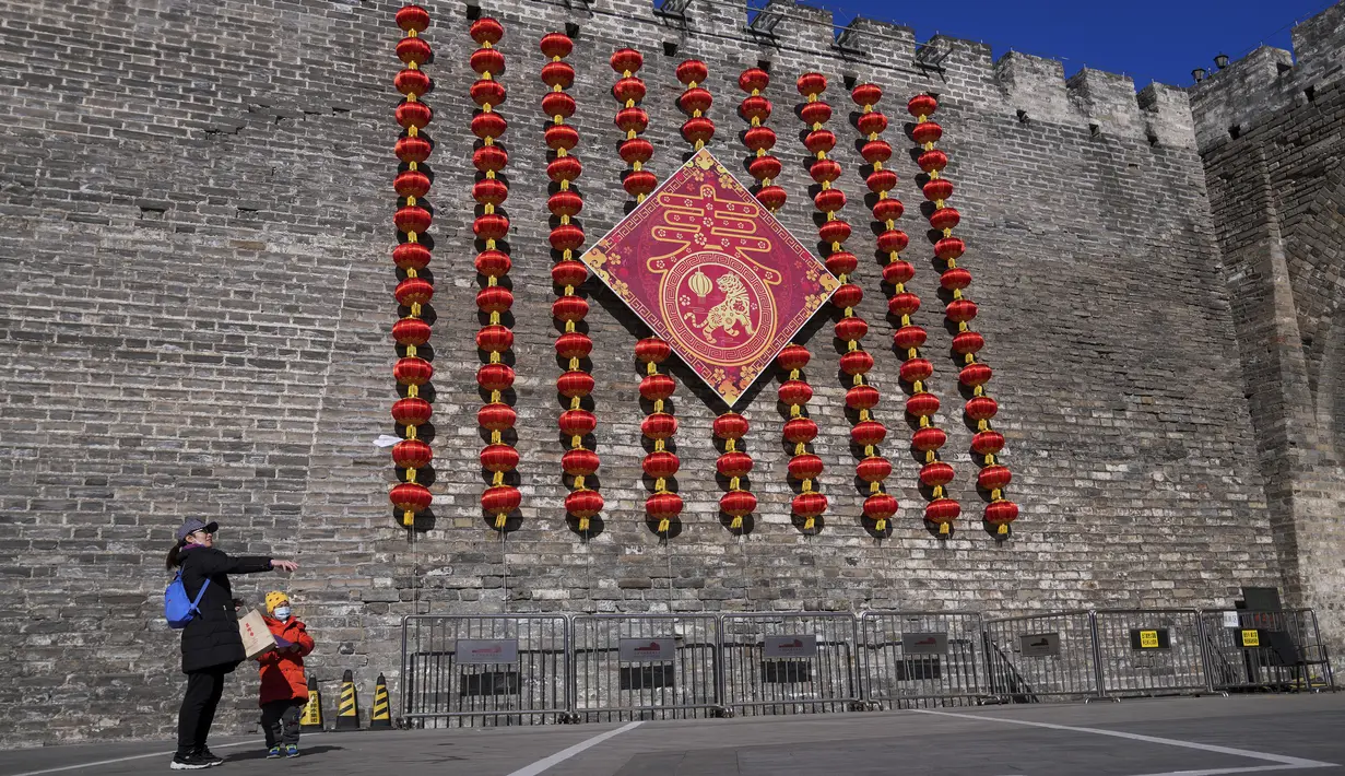 Seorang wanita dan anak  bermain dengan pesawat kertas di dekat dekorasi lentera untuk Tahun Baru Imlek jelang Tahun Baru Imlek di di sisa-sisa tembok kota di Beijing, Kamis (27/1/2022). (AP Photo/Andy Wong)