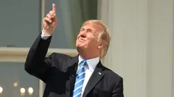 Presiden Amerika Serikat (AS) Donald Trump menunjuk ke atas saat menyaksikan  gerhana matahari dari balkon Gedung Putih di Washington, Senin (21/8). Trump tampak menatap langsung ke arah matahari dengan mata telanjang. (AP Photo/Andrew Harnik)