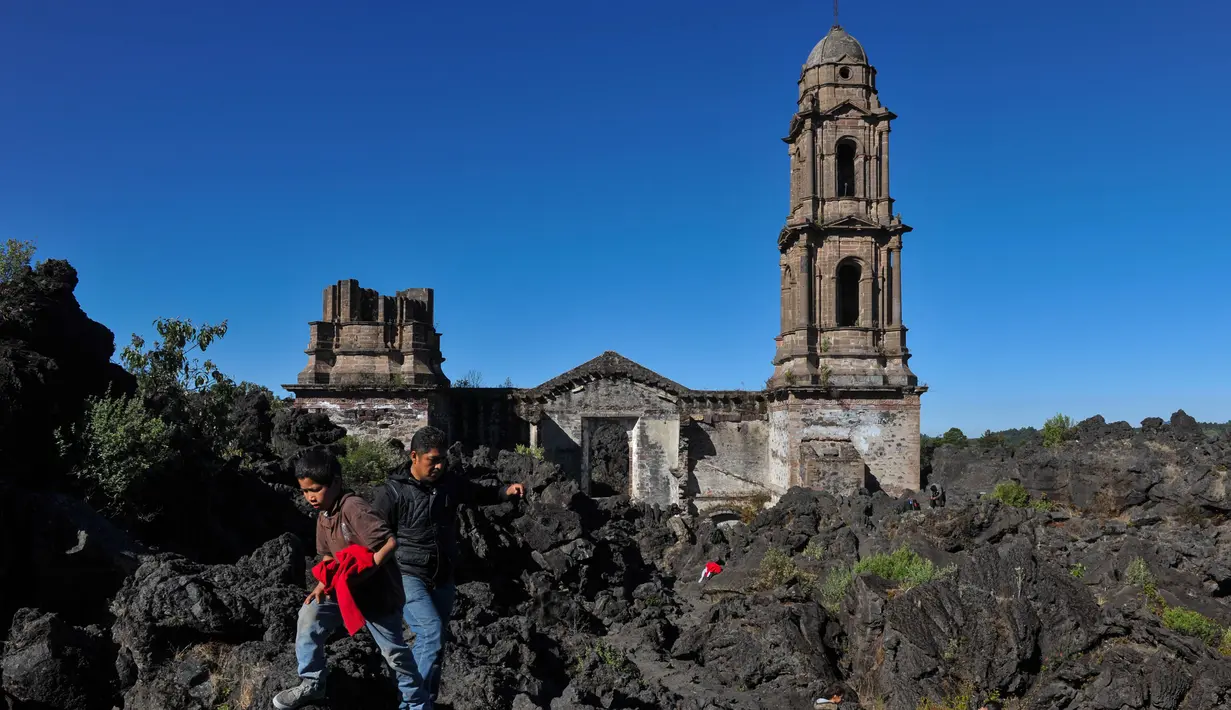 Wisatawan berjalan di dekat gereja San Juan Parangaricutiru di Angahuan, Meksiko, 17 Januari 2016. Gereja ini disebut sebagai keajaiban Tuhan karena luput dari sapuan lava gunung berapi pada  20 februari 1943 silam. (AFP PHOTO / Mario Vazquez)