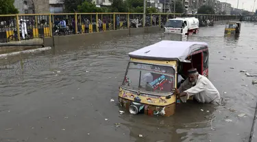 Seorang pengemudi mendorong bajaj saat melewati jalan yang banjir di Karachi, Pakistan, Kamis (23/9/2021). Banjir merendam Karachi setelah diguyur hujan deras. (AP Photo/Fareed Khan)