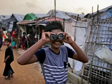 Seorang bocah Rohingya melihat melalui teropong mainan pada perayaan Idul Adha di kamp pengungsi Kutupalong, Bangladesh, Rabu (22/8). Hampir setahun mereka menghuni kamp ini usai kabur menghindari represi militer di Negara Bagian Rakhine. (AP/Altaf Qadri)