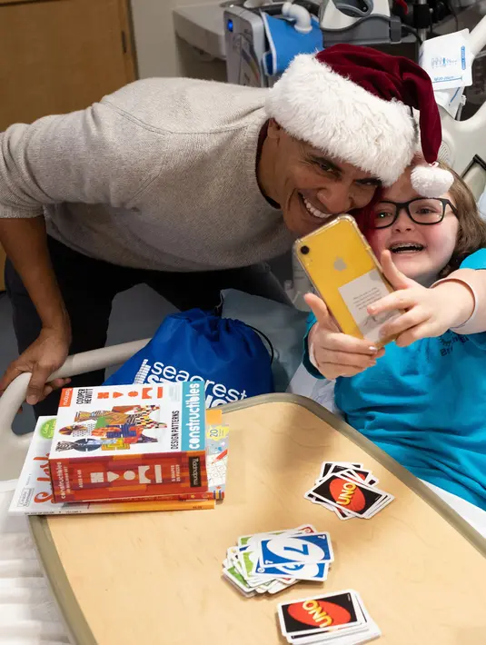 Mantan Presiden AS, Barack Obama berswafoto dengan seorang pasien anak di Children's National Medical Center , Washington, Rabu (19/12). Obama mengunjungi anak-anak yang sedang menjalani perawatan di sana untuk membagikan kado Natal. (Chuck Kennedy / AFP)