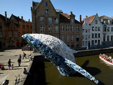 Sebuah perahu wisatawan berlayar melewati instalasi patung paus yang ditampilkan di sungai Brugges, Belgia, Sabtu (14/7). Patung paus berukuran 12 meter itu terbuat dari 5 ton sampah plastik yang mengambang di Samudra Pasifik dan Atlantik. (AFP/JOHN THYS)
