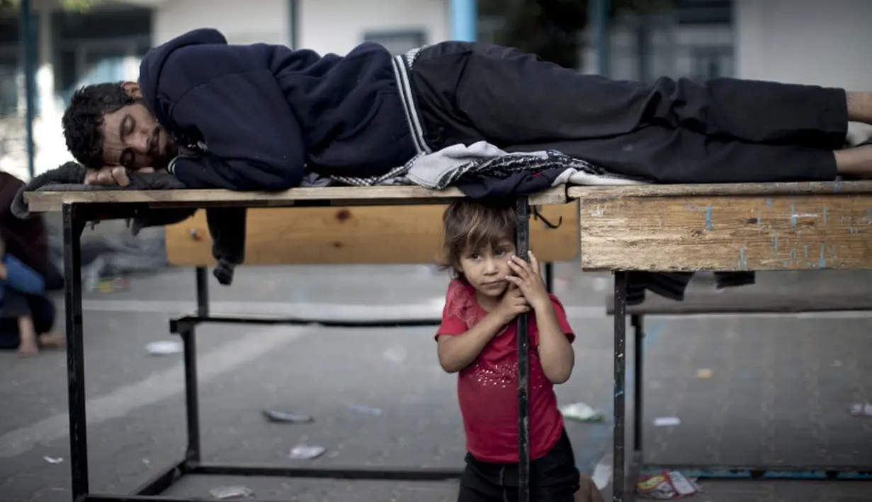 Seorang gadis kecil menjaga ayahnya yang sedang tertidur pulas di tempat pengungsian. Mereka meninggalkan rumah karena mendapat ancaman akan dibom (15/07/2014) (AFP PHOTO/MAHMUD HAMS)
