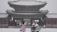 Pengunjung yang mengenakan masker untuk membantu mengekang penyebaran virus corona berfoto di tengah salju di Istana Gyeongbok, salah satu landmark terkenal Korea Selatan, di Seoul, Korea Selatan, Rabu (19/1/2022). (AP Photo/Lee Jin-man)