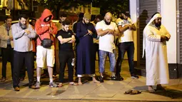 Sejumlah pria muslim melaksanakan salat di lokasi sebuah van yang menabrak pejalan kaki di Finsbury Park Road, London utara, Senin (19/6). Polisi menyebut van menabrak kerumunan orang yang baru selesai salat di masjid Finsbury Park (Yui Mok/PA via AP)