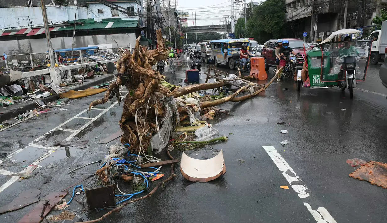 Pengendara kendaraan bermotor melewati batang pohon yang tergeletak di salah satu jalan di Manila, Filipina pada 25 Juli 2024. (TED ALJIBE/AFP)