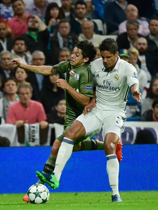 Bek Real Madrid, Raphael Varane berusaha merebut bola dari elandang Legia Warsawa, Guilherme Marques pada Liga Champion di stadion Santiago Bernabeu, Spanyol, (18/10). Madrid menang telak atas Legia dengan skor 5-1. (AFP Photo/Pierre-Philippe Marcou)