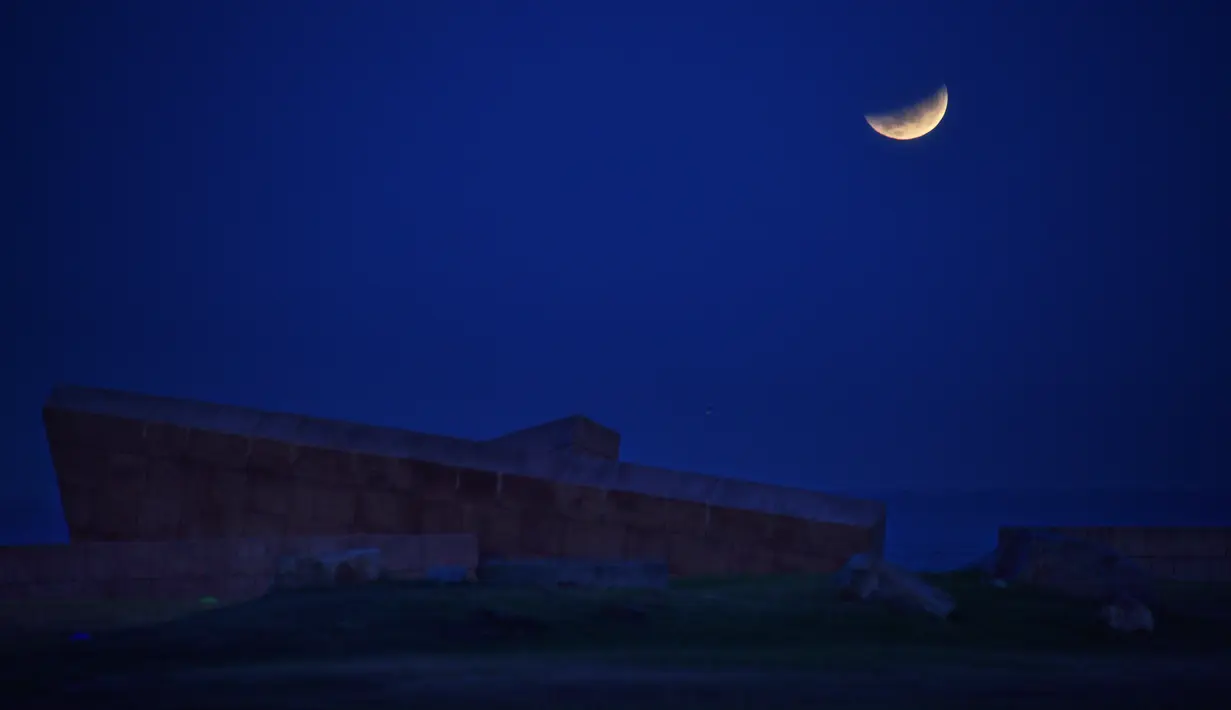 Bulan purnama yang sebagian gerhana terlihat tepat sebelum terbenam di belakang Holocaust Memorial di Montevideo, Uruguay pada Rabu (26/5/2021). (Mariana SUAREZ / AFP)