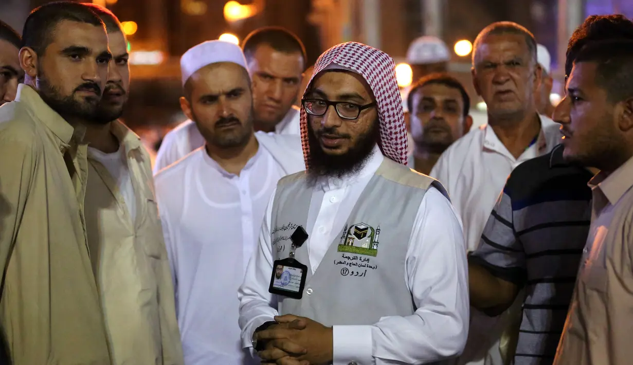 Jemaah haji berbincang dengan seorang penerjemah di kota suci Islam, Makkah, Arab Saudi, 17 Agustus 2018. Para penerjemah ini bisa dicirikan dengan pria yang memakai rompi abu-abu, dan di dadanya dibordir nama bahasa yang dia kuasai. (AFP/AHMAD AL-RUBAYE)