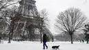 Seorang pria membawa anjingnya berjalan di bawah Menara Eiffel di Paris, Prancis (7/2). Ratusan orang terpaksa meninggalkan mobil mereka untuk tidur di tempat penampungan darurat akibat cuaca ekstrem yang melanda. (AFP Photo / Thomas Samson)