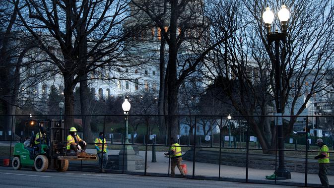 Pekerja memasang pagar pengendali kerumunan di sekitar Capitol Hill sehari setelah massa pendukung Donald Trump menerobos masuk ke Gedung Capitol, Washington, DC. Kamis (7/1/2021). Serangan dilakukan saat para anggota Kongres hendak mengesahkan kemenangan Joe Biden. (Brendan Smialowski/AFP)