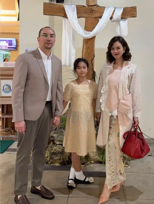 Astrid Tiar mengenakan atasan kebaya modern warna putih pink dipadukan kain batik lilin sambil membawa tas merah. [@astridtiar127]