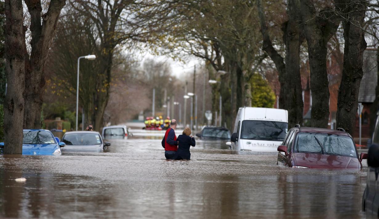 Warga melintasi banjir yang merendam pemukiman Warwick Road Carlisle, Inggris, Minggu (6/12). Puluhan ribu rumah tidak punya listrik karena Badai Desmond yang menyebabkan banjir di Inggris utara dan sebagian Skotlandia. (REUTERS/Phil Noble)