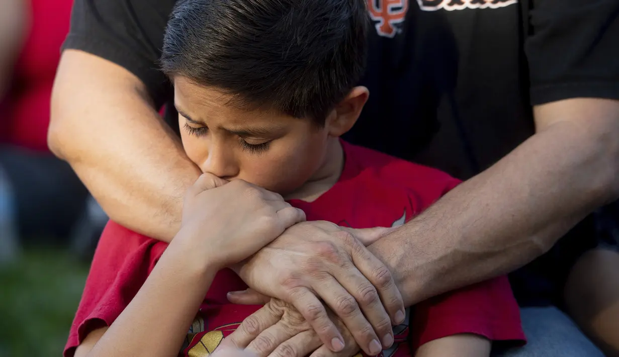 Seorang anak memegang tangan ayahnya saat menghadiri acara berjaga-jaga untuk korban penembakan brutal di festival kuliner Gilroy Garlic di Gilroy, California (29/7/2019). Dalam kejadian tersebut polisi berhasil menembak palaku penyerangan. (AP Photo/Noah Berger)