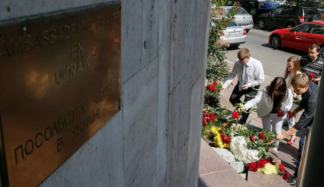 Sejumlah orang menaruh bunga di depan Kedutaan Besar Prancis di Kiev, Ukraina, (15/7). Karangan bunga tersebut untuk menghormati para korban teror Truk Maut saat perayaan hari Bastille di Nice. (REUTERS/Gleb Garanich)
