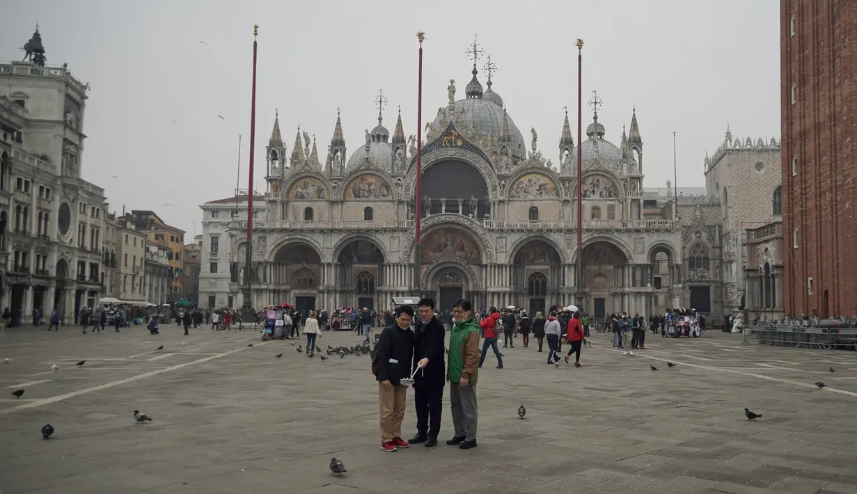 Wisatawan mengenakan masker pelindung saat berswafoto di Alun-Alun St. Mark di Venesia, Italia, Selasa (25/2/2020). Hingga kini, setidaknya 272 orang telah terinfeksi virus corona atau COVID-19 di Italia. (AP Photo/Renata Brito)