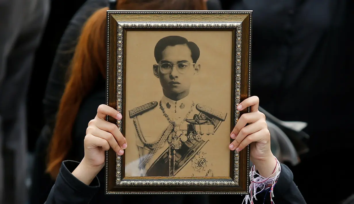 Seorang pelayat wanita memegang foto Raja Bhumibol Adulyadej saat berkumpul di luar Grand Palace sambil menyanyikan rekaman lagu kerajaan untuk menghormati raja mereka, di Bangkok, Thailand, (22/10) (REUTERS/Jorge Silva)
