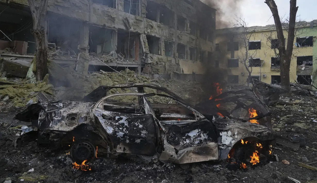 Sebuah mobil terbakar di sisi rumah sakit bersalin yang rusak akibat serangan udara di Mariupol, Ukraina (9/2/2022). Serangan Rusia telah merusak parah sebuah rumah sakit bersalin di kota pelabuhan Mariupol yang terkepung, kata pejabat Ukraina. (AP Photo/Evgeniy Maloletka)