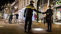 Polisi mengontrol sertifikasi keluar pada orang yang lewat saat jam malam dimulai di Haarlem, Belanda (23/1/2021). Belanda memasuki fase terberat dari pembatasan anti-virus Corona hingga saat ini. (AFP/ANP/Koen van Weel)