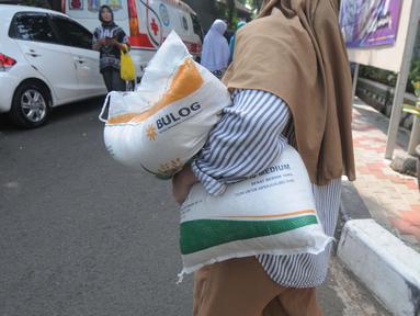 Warga berjalan dengan membawa beras kemasan 10 kilogram di Kelurahan Pela Mampang, Jakarta, Jumat (3/5/2024). (merdeka.com/Imam Buhori)