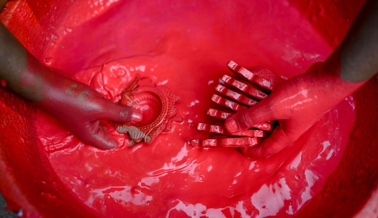 Seorang pembuat tembikar mewarnai lampu tanah jelang Festival Diwali di sepanjang pinggir jalan di New Delhi, India, 18 Oktober 2022. Festival Diwali atau dalam agama Hindu berarti Festival Cahaya melambangkan kemenangan baik atas keburukan, dan lampu atau pelita dinyalakan sebagai tanda perayaan serta harapan umat manusia. (Sajjad HUSSAIN/AFP)