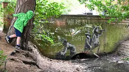 Stensil anak-anak yang bermain menjadi pelaut menjadi subjek karya seni grafiti yang menampilkan ciri-ciri seniman jalanan Banksy di dinding jembatan di Everitt Park di Lowestoft di pantai timur Inggris pada 8 Agustus 2021. Karya tersebut belum diklaim oleh Banksy. (JUSTIN TALLIS / AFP)