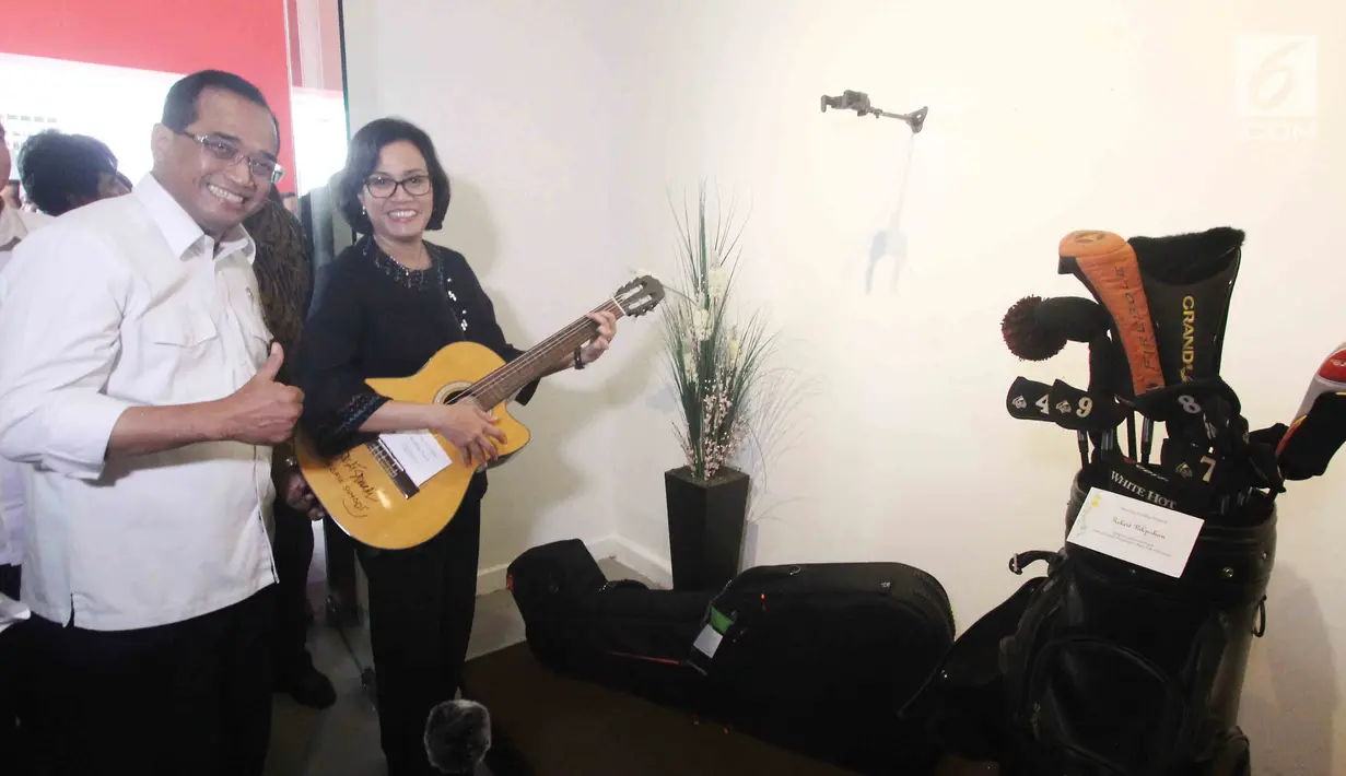 Menkeu Sri Mulyani berpose sambil memegang gitar didampingi Menhub Budi Karya dalam pameran barang yang di lelang di Galeri Nasional, Jakarta, Rabu (28/2). (Liputan6.com/Angga Yuniar)